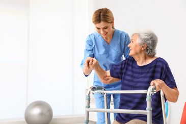 Foto: Pflegekraft hilft älterer Frau mit Gehhilfe